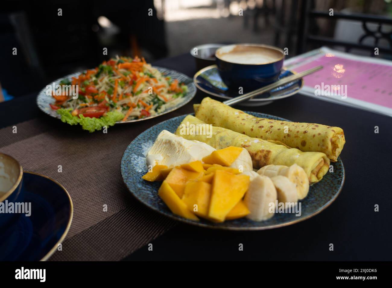 Deliziosa colazione dello Sri Lanka su un tavolo di legno. Pancake con frutta e gelato, spaghetti vegetali e cappuccino. Foto Stock