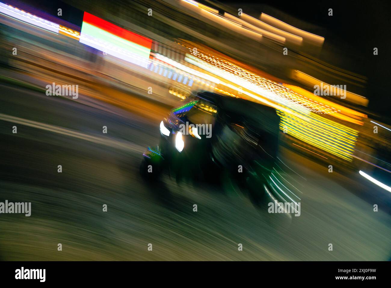 Un risciò verde che si muove rapidamente attraverso una strada illuminata della città di notte. Foto Stock