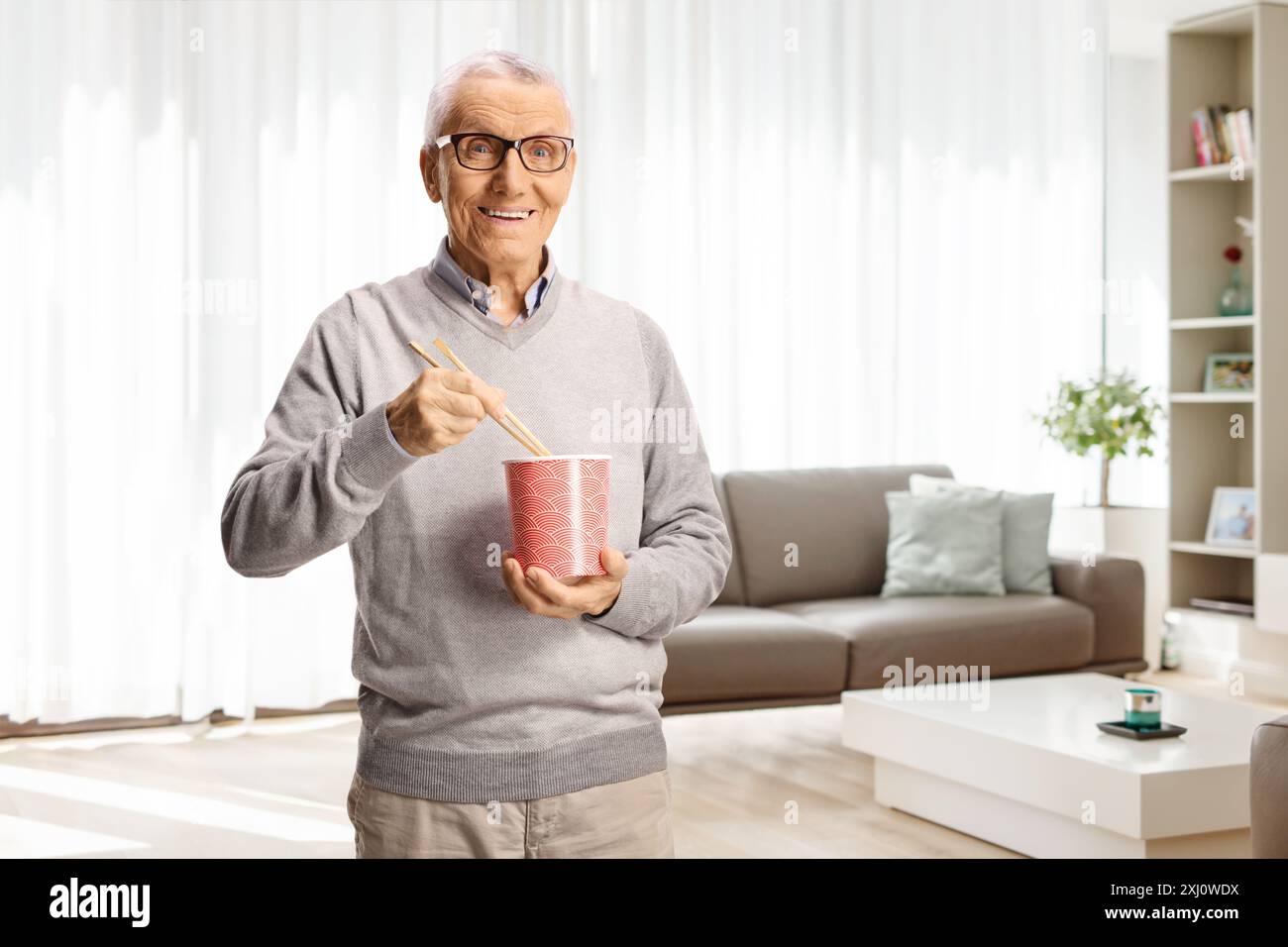 Uomo anziano che tiene una scatola e mangia spaghetti a casa Foto Stock