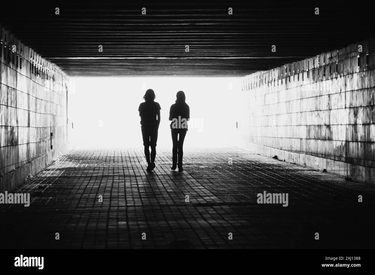 Sagome di due persone in un tunnel. Immagine in bianco e nero con luce proveniente da dietro. Coppia che si allontana dalla telecamera. Foto Stock