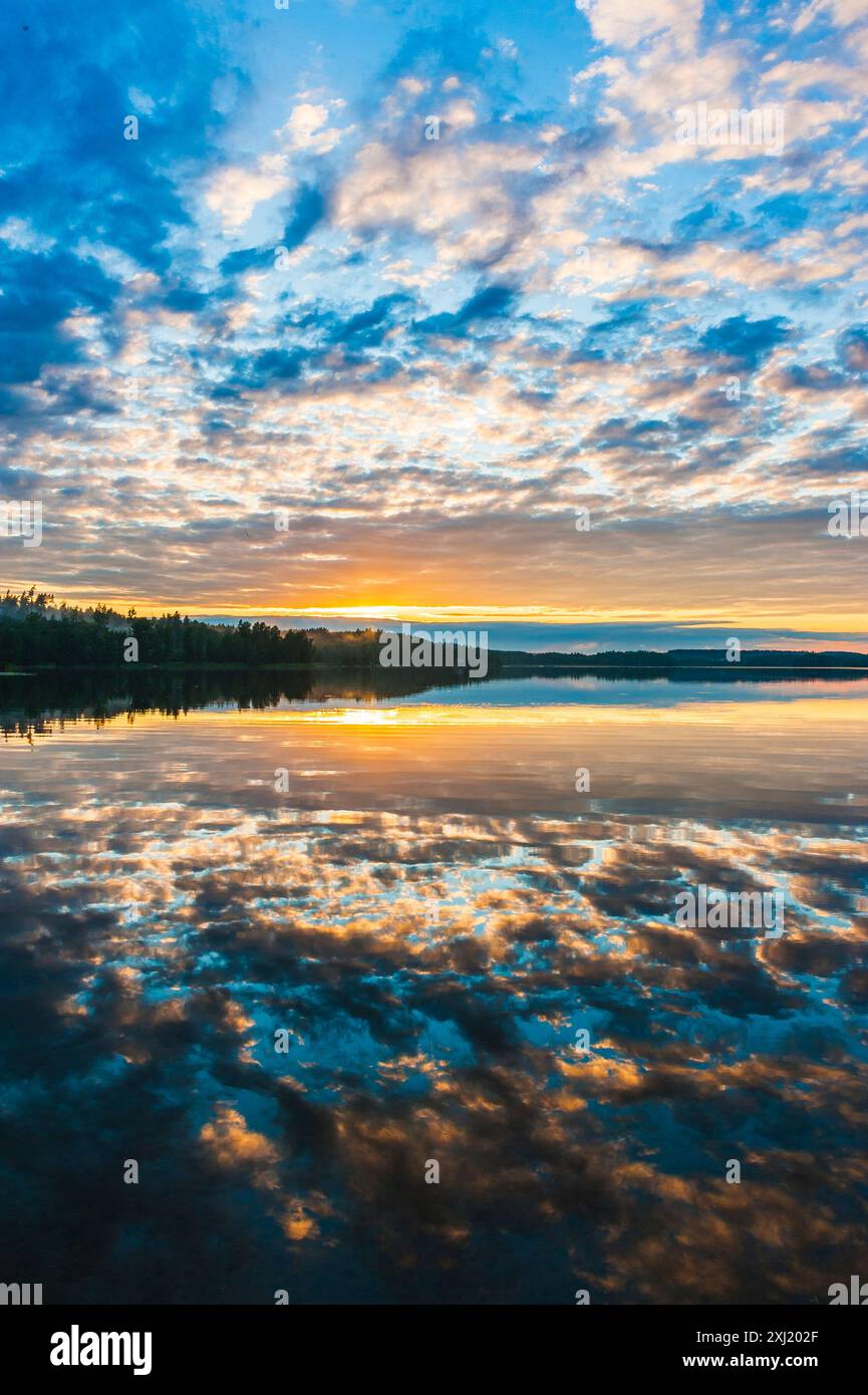 Un pittoresco tramonto su un tranquillo lago svedese, con nuvole colorate che si riflettono sull'acqua ferma. Il cielo è un bel mix di blu, arancione e. Foto Stock