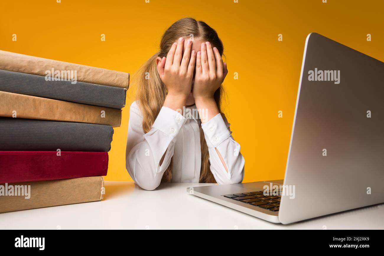 Scuola elementare ragazza grida che ricopre la faccia con le mani, sfondo giallo Foto Stock
