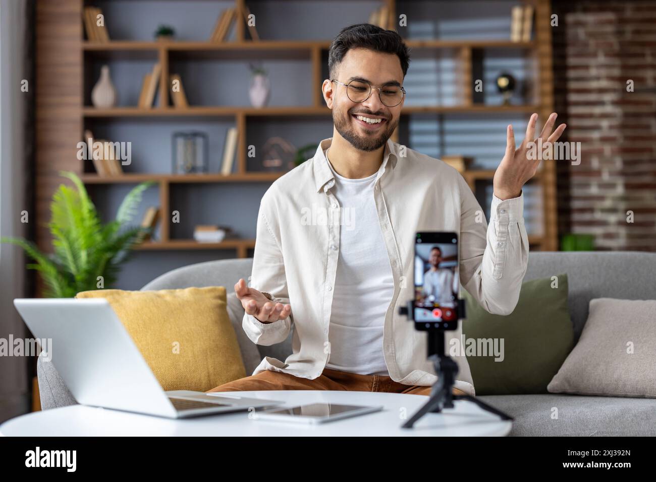 Comodo a casa, un uomo indiano si impegna con il suo pubblico attraverso un vlog. Il suo carisma naturale riempie l'accogliente salotto mentre registra sul suo smartphone, creando contenuti personali e leggibili. Foto Stock