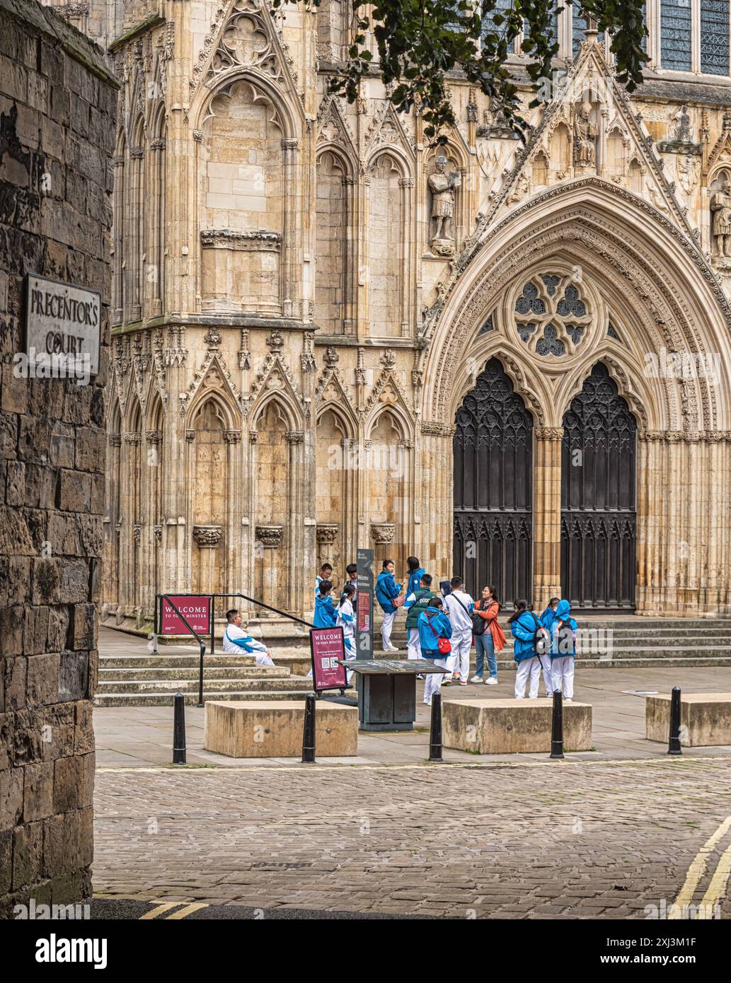 Una vista dell'ingresso alla York Minster, dove si riuniscono giovani studenti in uniforme blu e bianca. Grandi porte doppie sono su un lato e la parete di un si Foto Stock