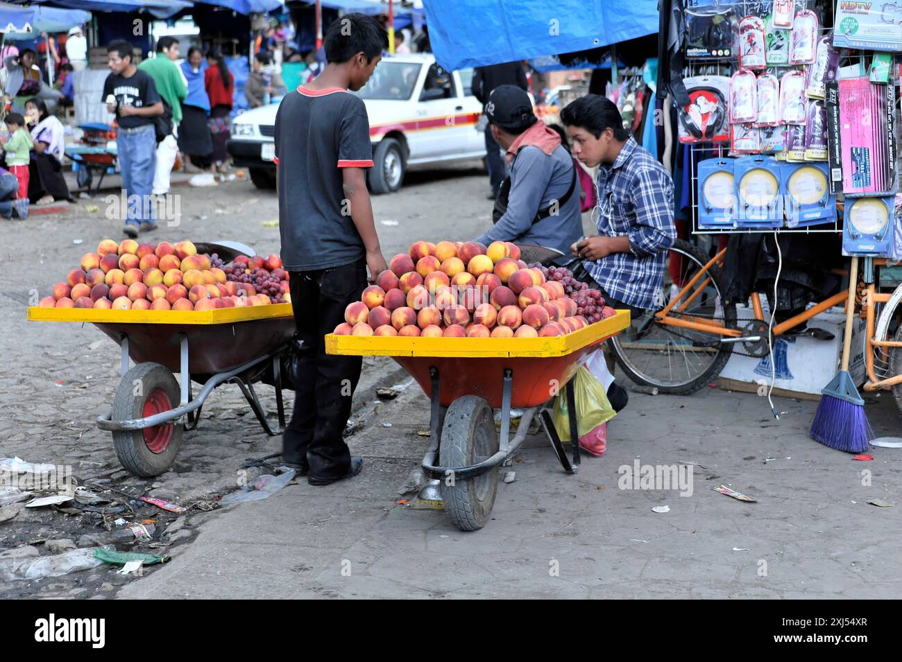 San Christobal de las Casas, Messico, America centrale, mercato con gente e carretti a mano pieni di pesche in una strada trafficata Foto Stock