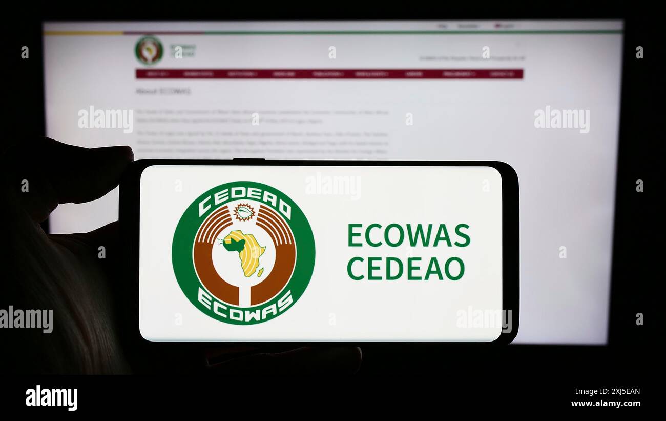 Stoccarda, Germania, 02-15-2024: Persona che detiene un cellulare con il logo della Comunità economica degli Stati dell'Africa occidentale (ECOWAS) davanti alla pagina web. Concentrati Foto Stock