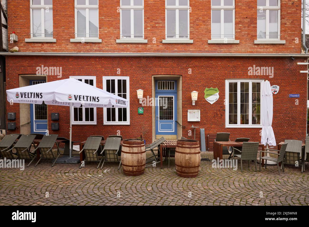 Area esterna di un ristorante con vecchie botti di birra come decorazione, tavoli e sedie ed anche un ombrellone con pubblicità Veltins Foto Stock