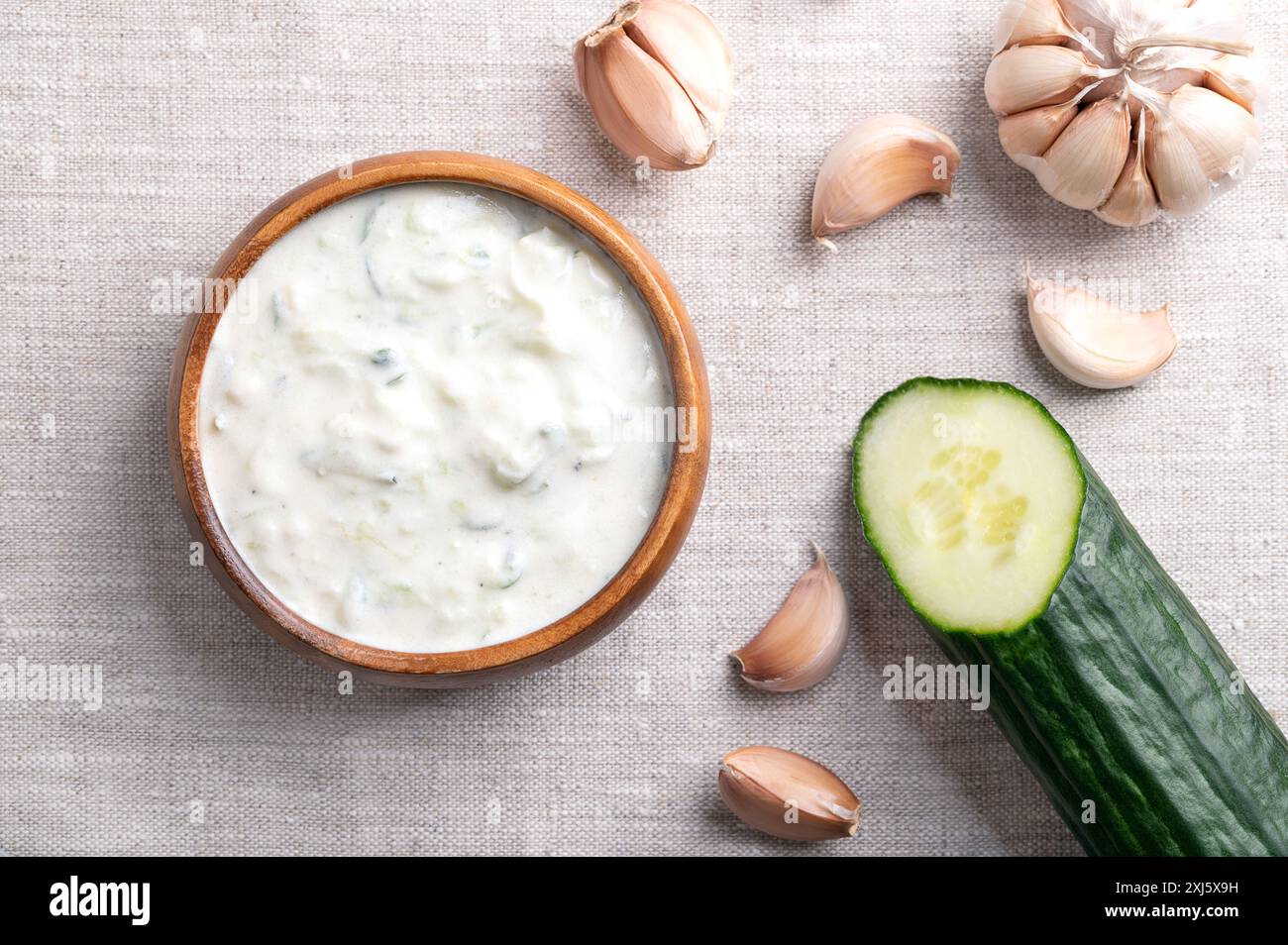 Tzatziki fresco in una ciotola di legno su tessuto di lino. Salsa rinfrescante, zuppa o salsa, fatta di yogurt affaticato salato, mescolato con cetrioli, aglio, ecc. Foto Stock