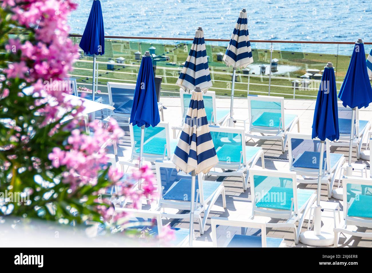 Un'invitante terrazza sul mare con file di lettini turchesi abbinati a eleganti ombrelloni a righe blu e bianche. Elegante relax Foto Stock