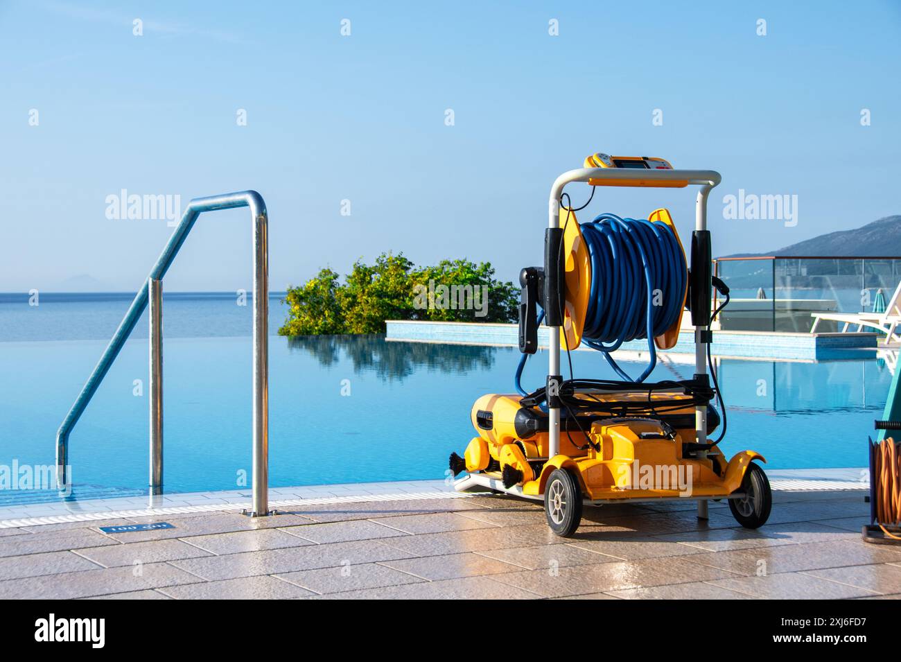 Il pulitore robotizzato della piscina si trovava sulla terrazza soleggiata accanto a una piscina a sfioro che si affacciava sul mare. Perfetto per mantenere l'acqua cristallina in una cacca di lusso Foto Stock