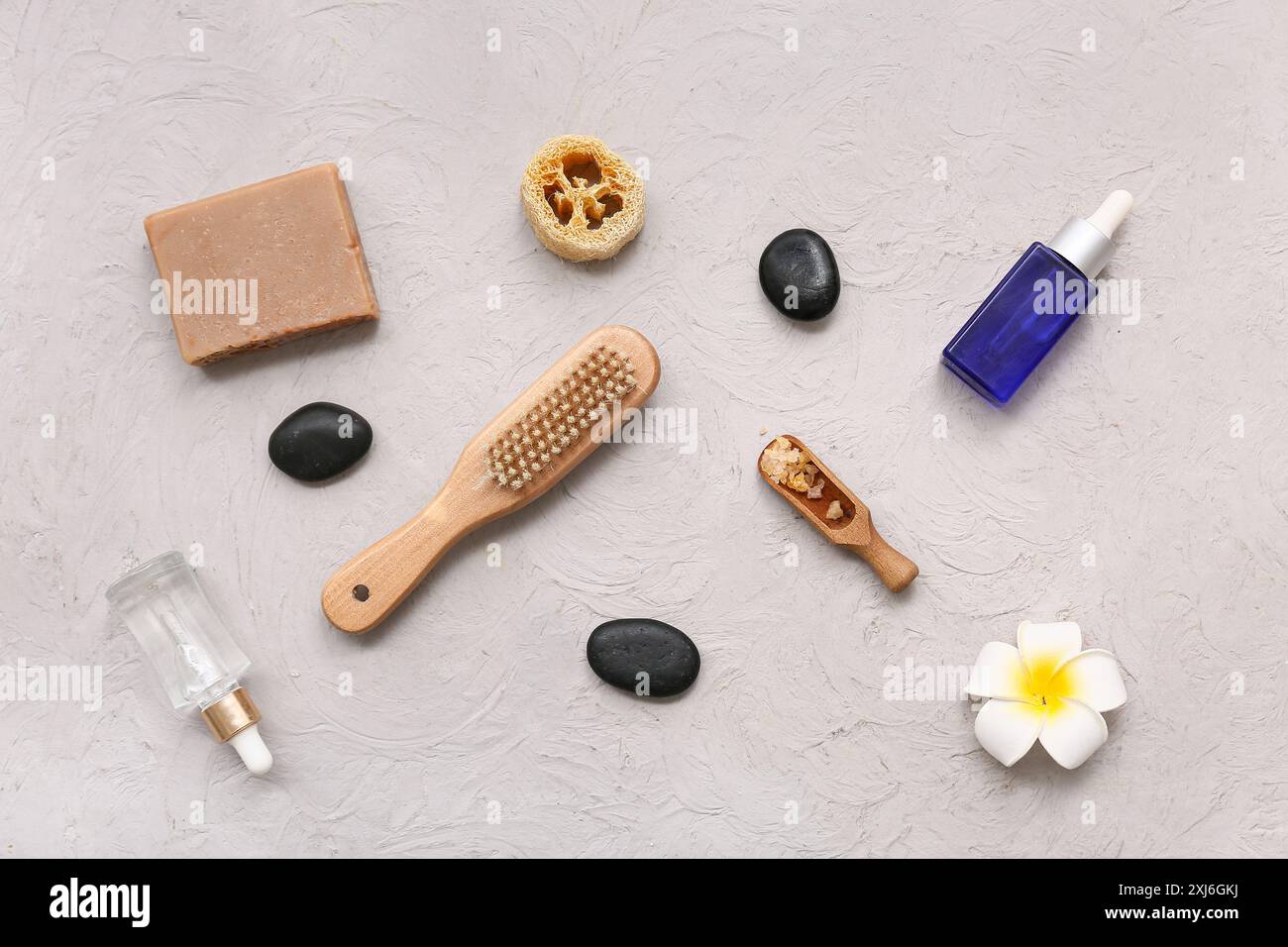 Splendida composizione con pietre termali, fiori di plumeria, sapone, loofah, bottiglie di olio essenziale e sale marino in paletta su sfondo grunge Foto Stock