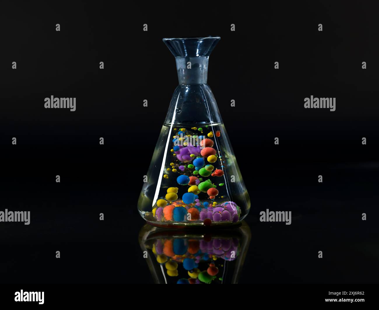 Sfere di olio di paraffina e vernice acrilica che galleggiano in un becher d'acqua Foto Stock