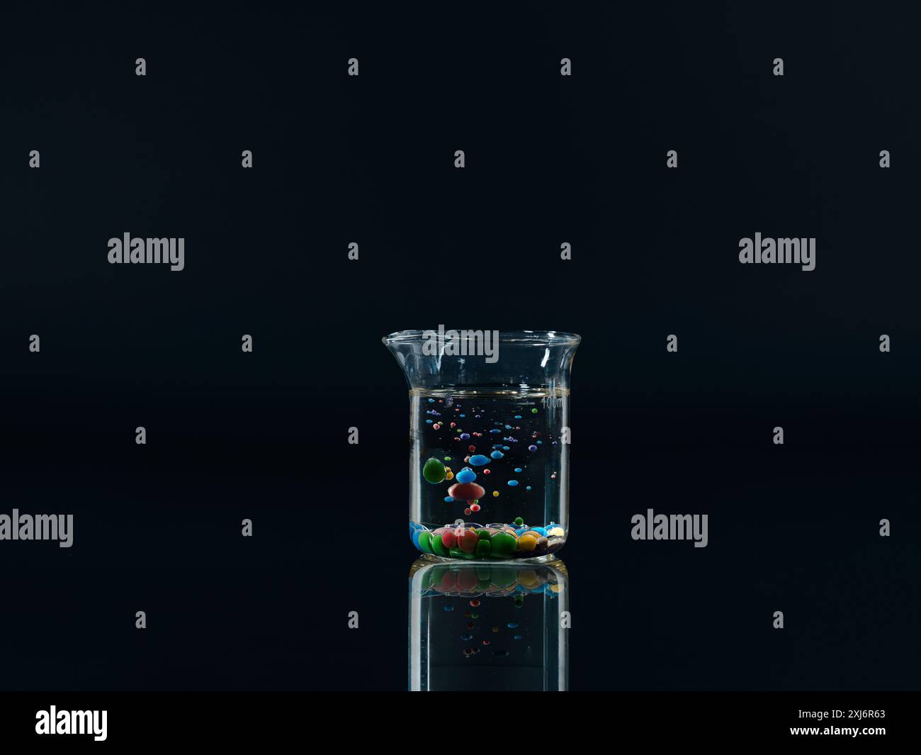 Sfere di olio di paraffina e vernice acrilica che galleggiano in un becher d'acqua Foto Stock