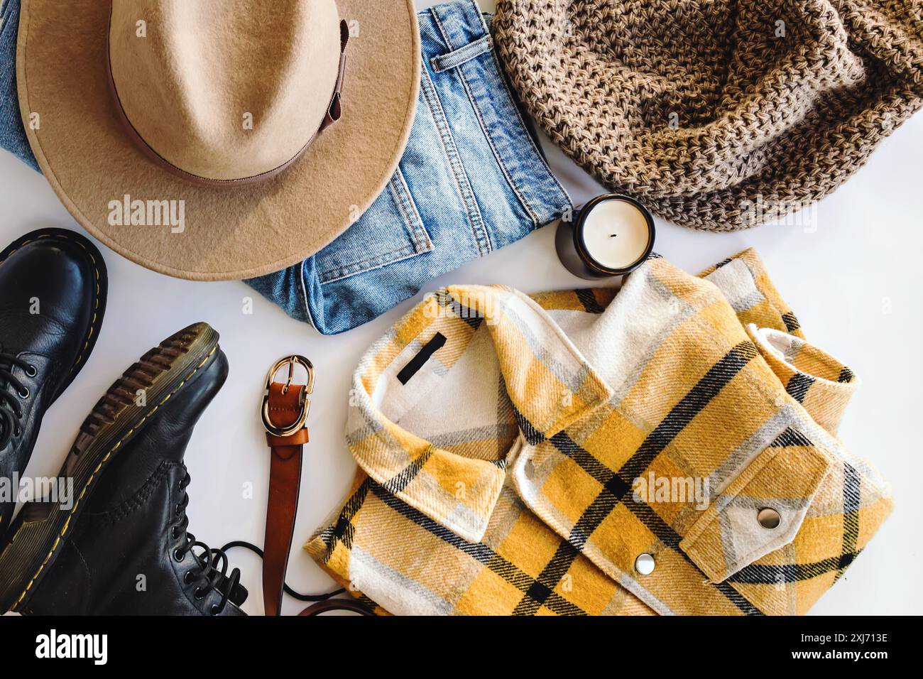 Modello piatto di indispensabili alla moda autunnali, tra cui un cappello beige, jeans in denim, una sciarpa a maglia e una camicia a quadri gialla Foto Stock