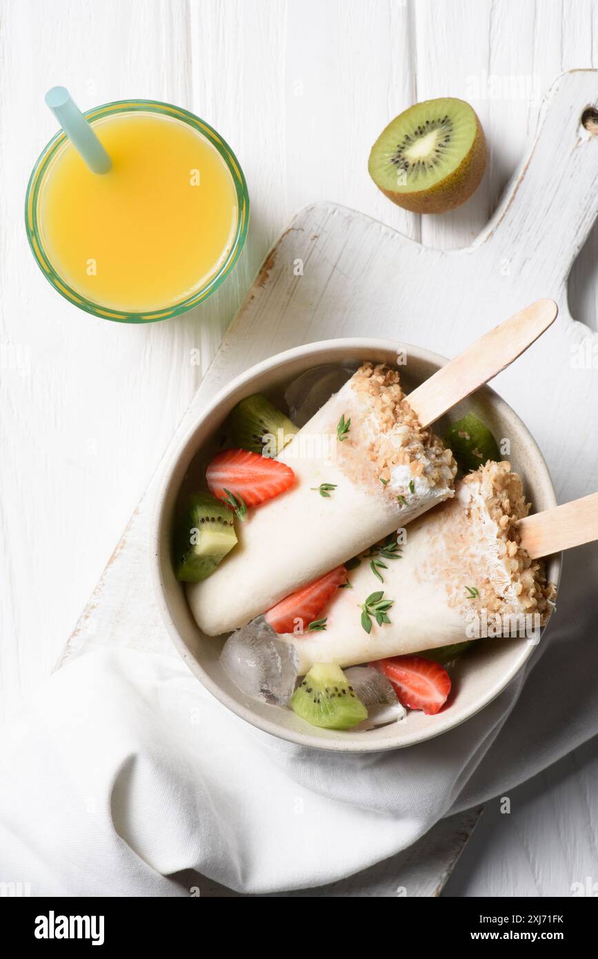 Frutta pop di ghiaccio con fragola e kiwi nella ciotola sul tavolo con succo di arancia Foto Stock