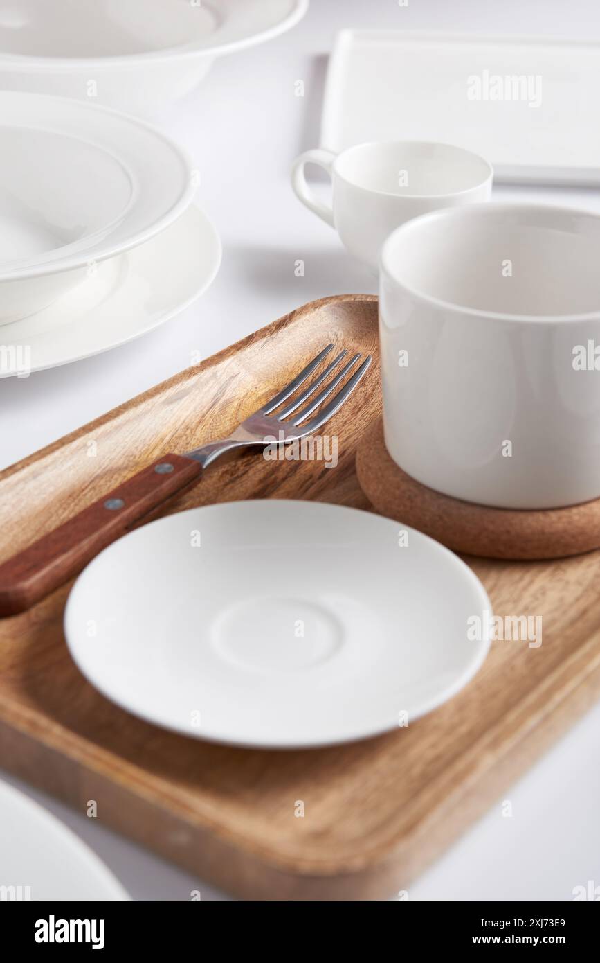 Messa a fuoco selettiva del vassoio in legno, forcella, varie piastre, Cup e della coppa sul tavolo bianco Foto Stock