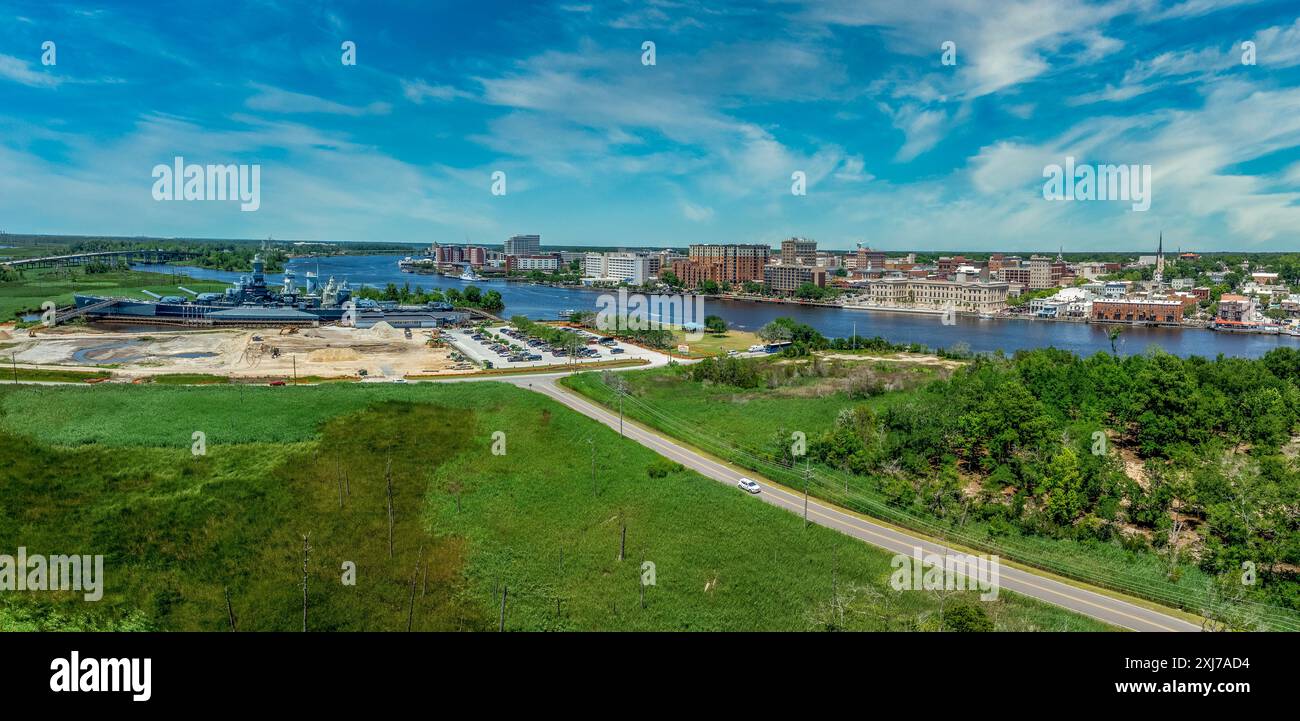 Vista panoramica aerea del quartiere storico di Wilmington, North Carolina, lungo il fiume Cape Fear, con la nave da battaglia del North Carolina con il cielo nuvoloso Foto Stock