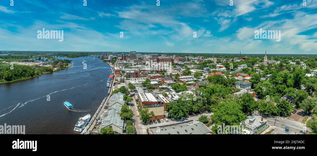 Vista panoramica aerea del quartiere storico di Wilmington, North Carolina, lungo il fiume Cape Fear, con la nave da battaglia del North Carolina con il cielo nuvoloso Foto Stock