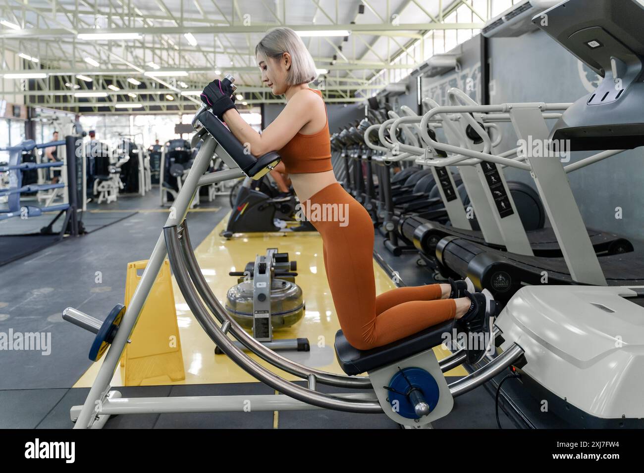 Giovane donna che usa la macchina da coaster ab durante il suo esercizio mattutino in una palestra locale Foto Stock