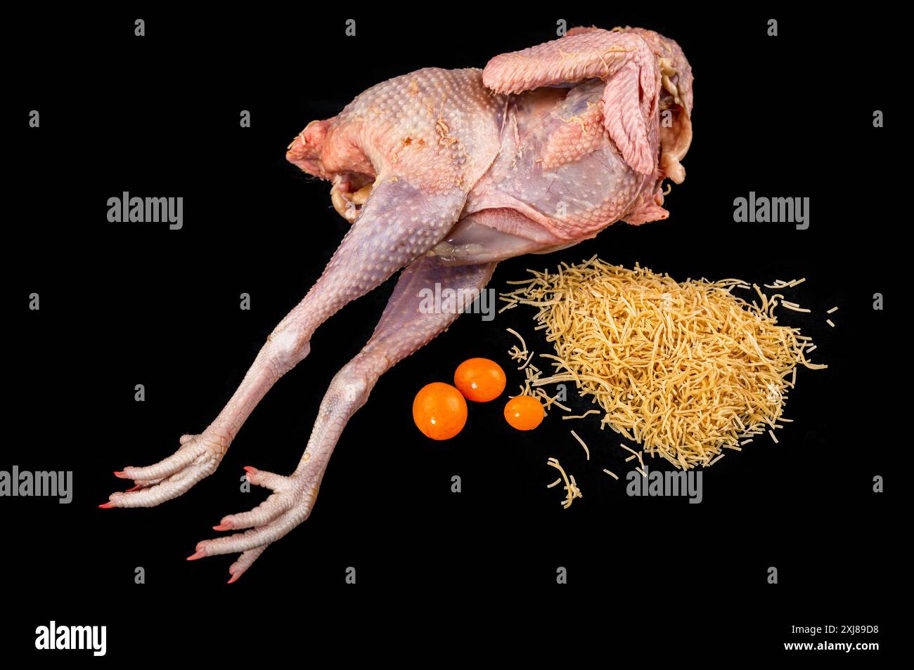 Corpo crudo di gallina senza testa, tre tuorli d'uovo e un mucchio di spaghetti disposti su sfondo nero. preparazione per bollire la zuppa, isolata, primo piano. Foto Stock