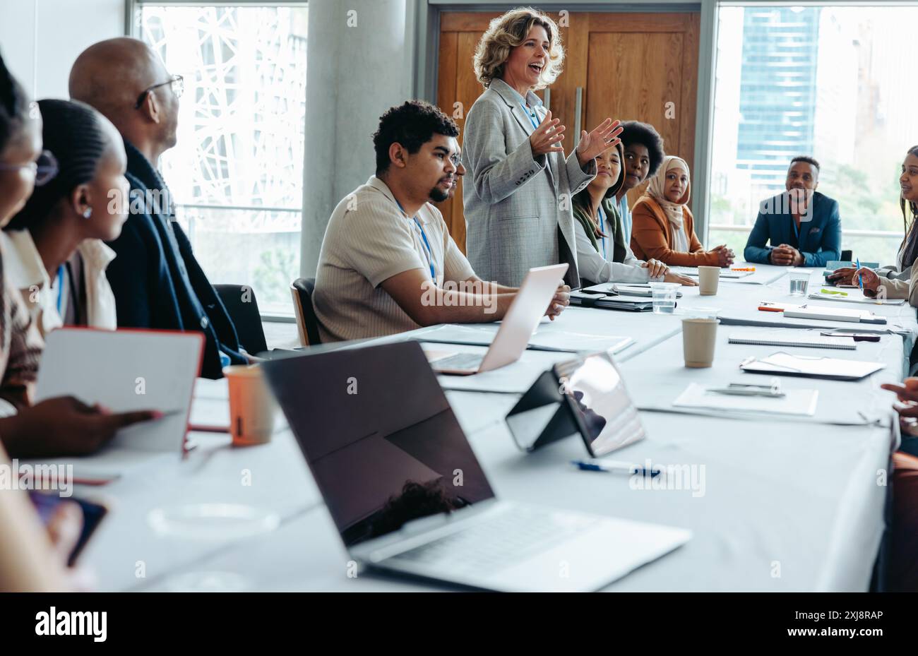 Donna sicura di sé che conduce una riunione d'affari in una sala riunioni con colleghi diversi, promuovendo il lavoro di squadra e la collaborazione in un ambiente di ufficio moderno. Foto Stock