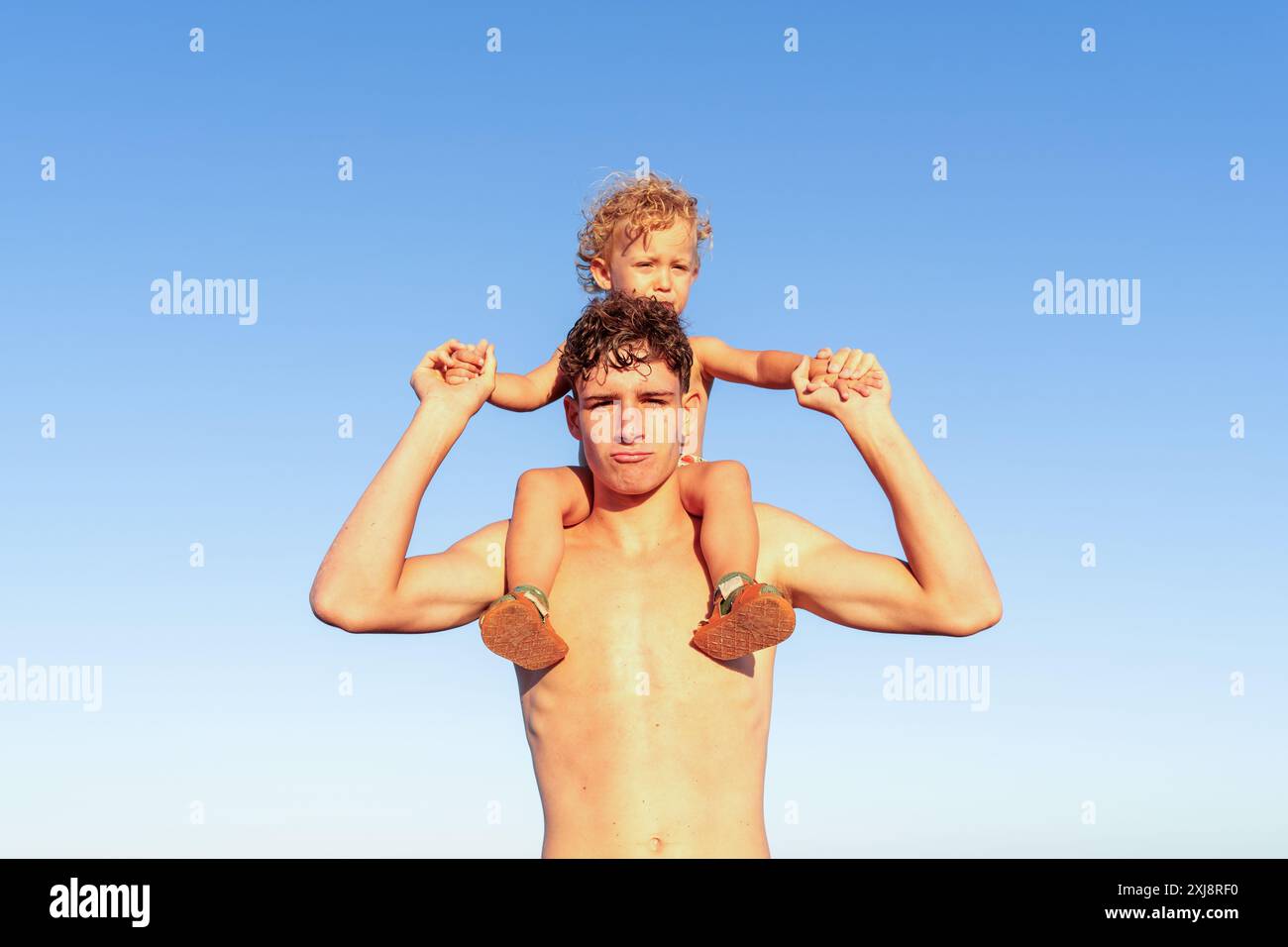 Giovane uomo che tiene il bambino contro il cielo azzurro trasparente sulla spiaggia Foto Stock