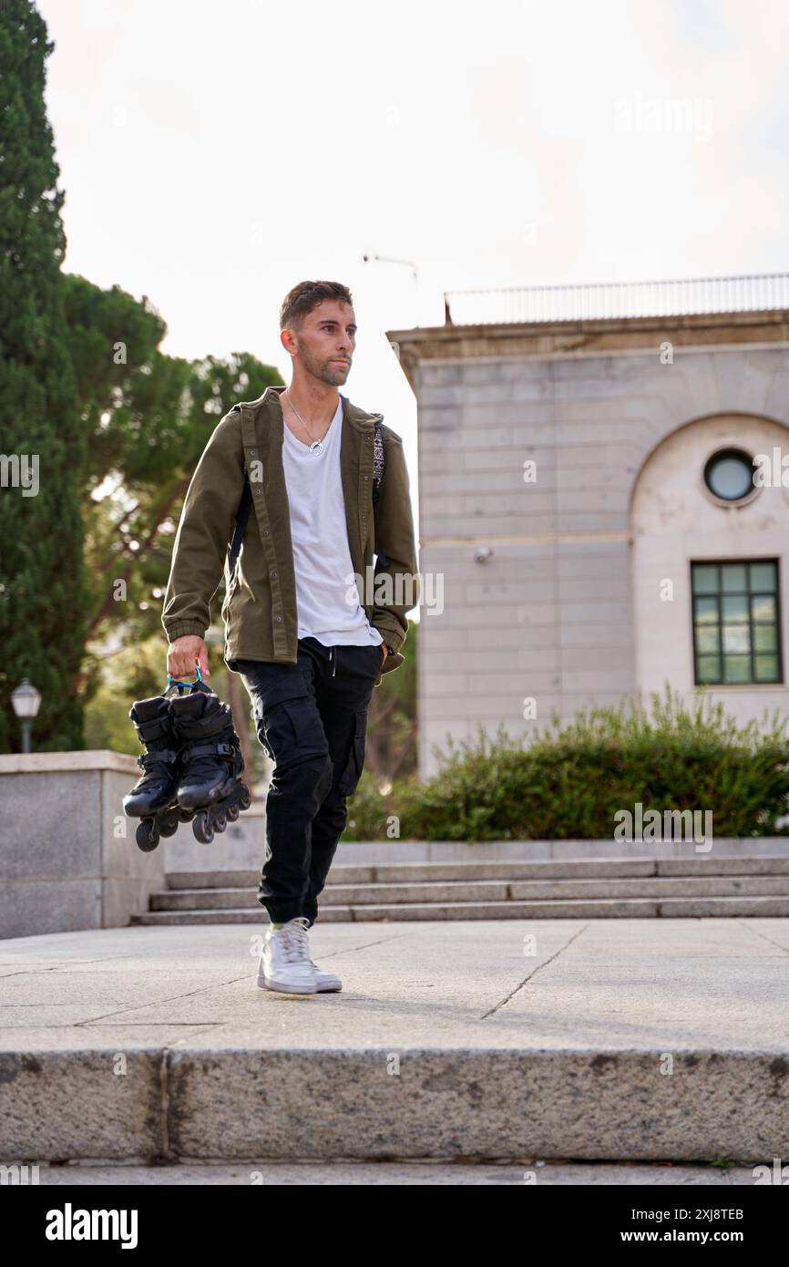 fotografia verticale di un giovane che cammina con un paio di pattini in linea in mano. Foto Stock