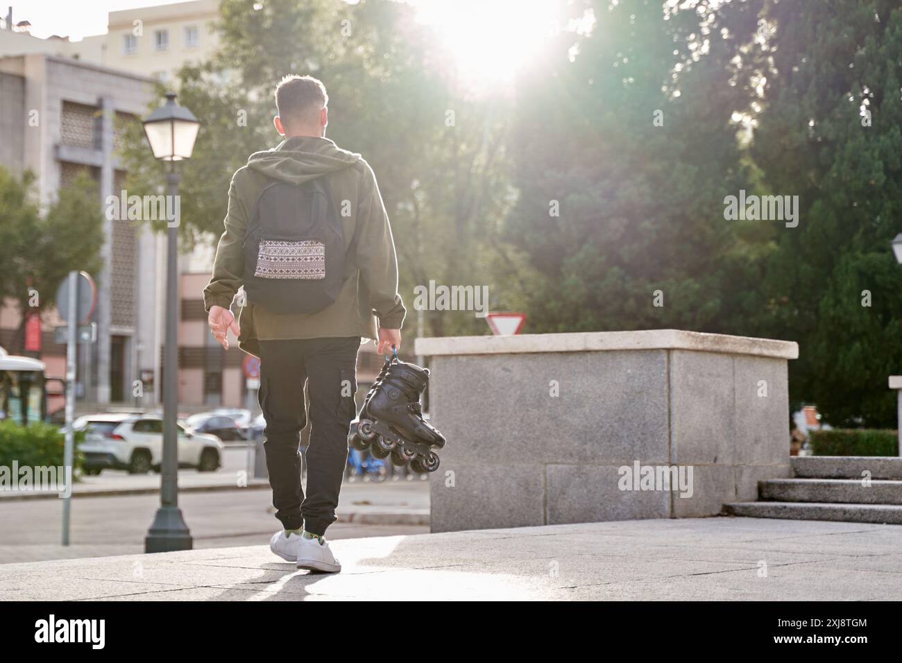 uomo che cammina per strada portando in mano i suoi pattini in linea Foto Stock