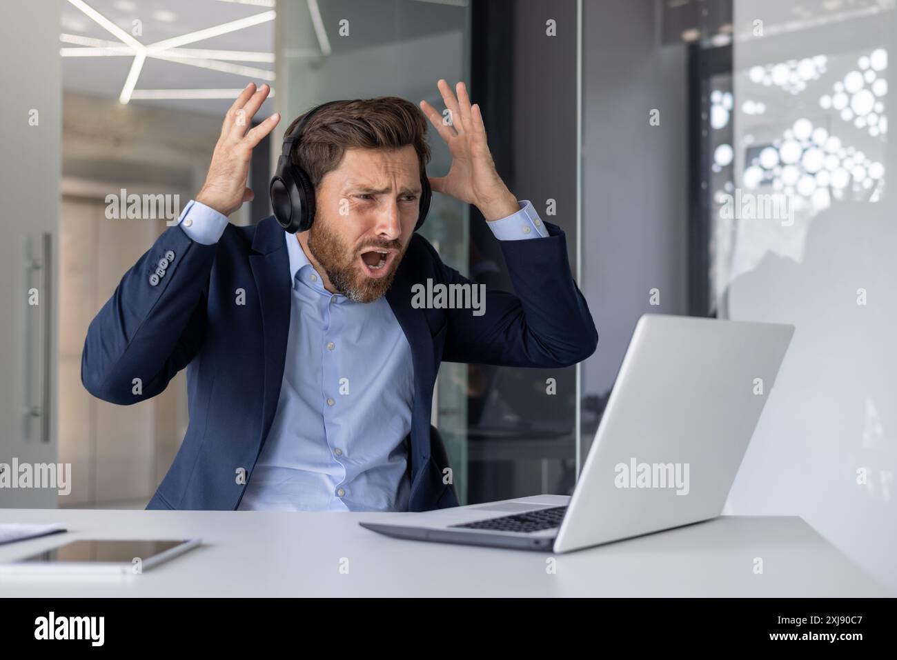 Un uomo d'affari frustrato reagisce mentre guarda una partita di sport online, mostrando confusione e delusione in un ufficio. Foto Stock