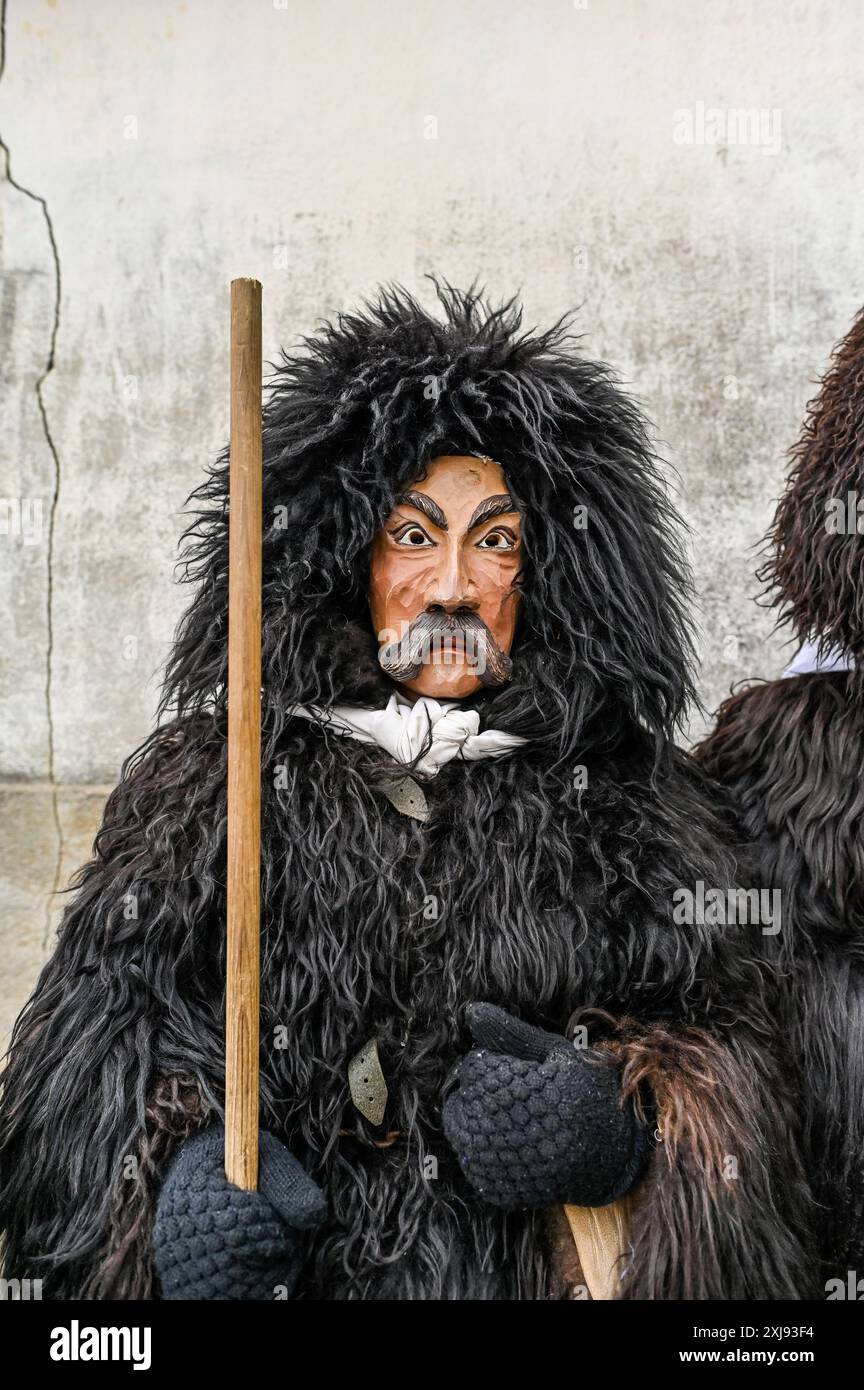 L'abbigliamento tradizionale del Carnevale di Sappada nelle Dolomiti è un'accattivante dimostrazione del ricco patrimonio culturale della regione. I partecipanti indossano costumi elaborati dai colori vivaci, ricami intricati e maschere in legno fatte a mano, ognuna realizzata in modo unico per rappresentare i vari personaggi del folklore locale. Il personaggio principale, Rollate, è particolarmente iconico: Una figura mascherata rivestita in pesante pelliccia di pecora scura con un grande cappuccio che copre completamente la testa, adornata da un ciuffo di lana rossa. La maschera di legno, con il suo aspetto poppa, baffi spessi scuri e sopracciglia, altera la voce del Foto Stock