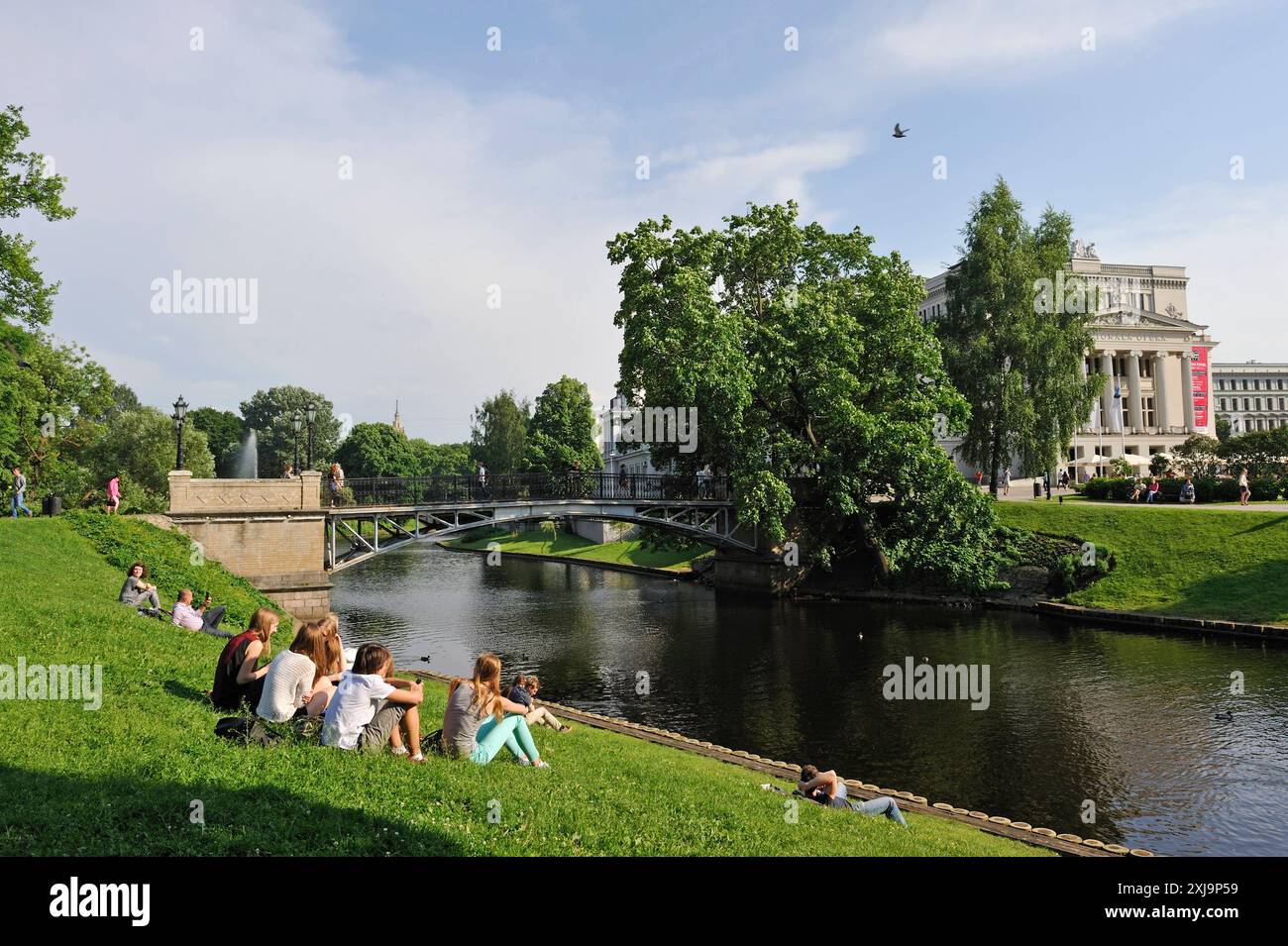 Giovani sulla riva del canale che circonda il centro storico di riga, di fronte al Teatro dell'Opera Nazionale, riga, Lettonia, regione del Baltico, Europe Copy Foto Stock