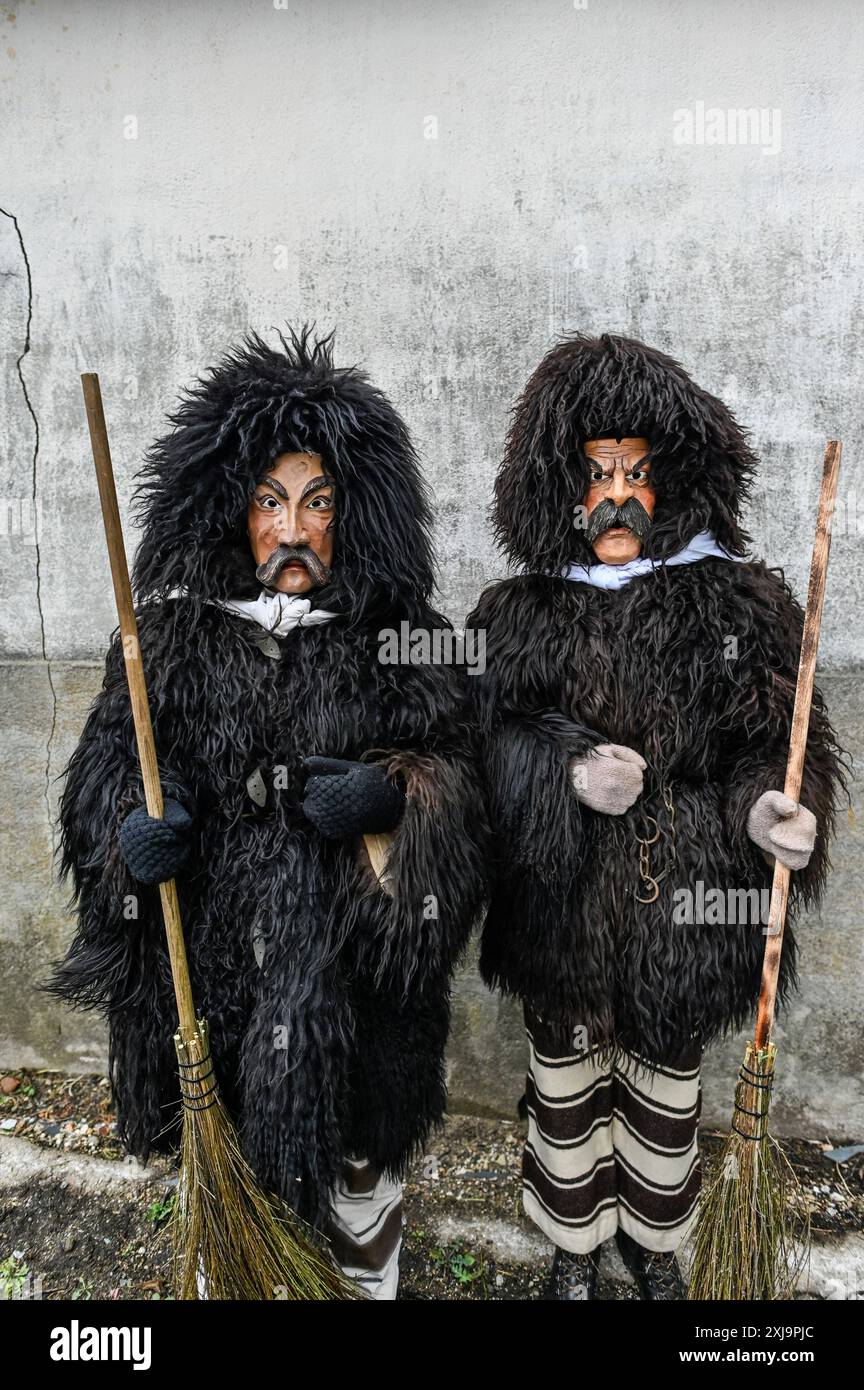L'abbigliamento tradizionale del Carnevale di Sappada nelle Dolomiti è un'accattivante dimostrazione del ricco patrimonio culturale della regione. I partecipanti indossano costumi elaborati dai colori vivaci, ricami intricati e maschere in legno fatte a mano, ognuna realizzata in modo unico per rappresentare i vari personaggi del folklore locale. Il personaggio principale, Rollate, è particolarmente iconico: Una figura mascherata rivestita in pesante pelliccia di pecora scura con un grande cappuccio che copre completamente la testa, adornata da un ciuffo di lana rossa. La maschera di legno, con il suo aspetto poppa, baffi spessi scuri e sopracciglia, altera la voce del Foto Stock