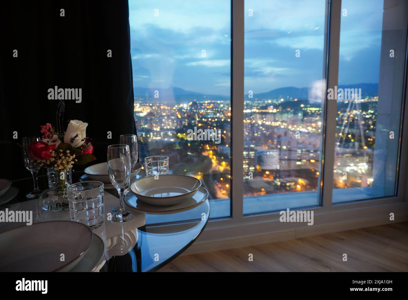 Romantico tavolo da pranzo di lusso accanto alla finestra con vista notturna sulla città in una camera d'hotel con appartamenti di lusso Foto Stock