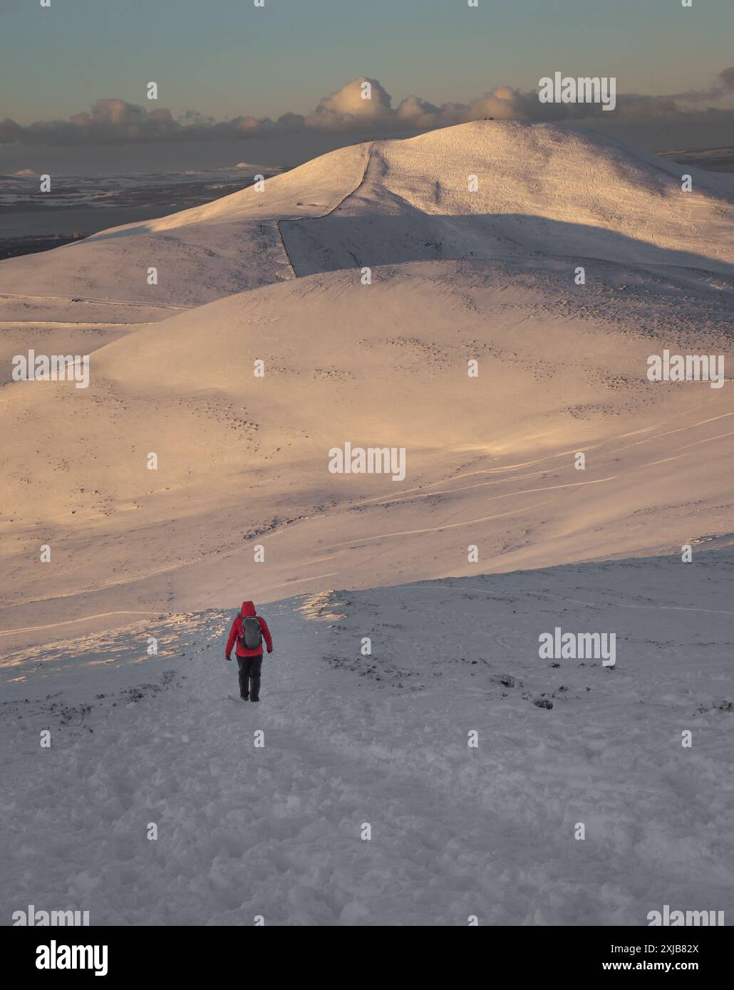 Persona che indossa una giacca rossa, uno zaino e abiti invernali, escursioni sulla cresta innevata delle montagne nelle colline di Pentland, vicino a Edimburgo, Scozia, nel wisconsin Foto Stock