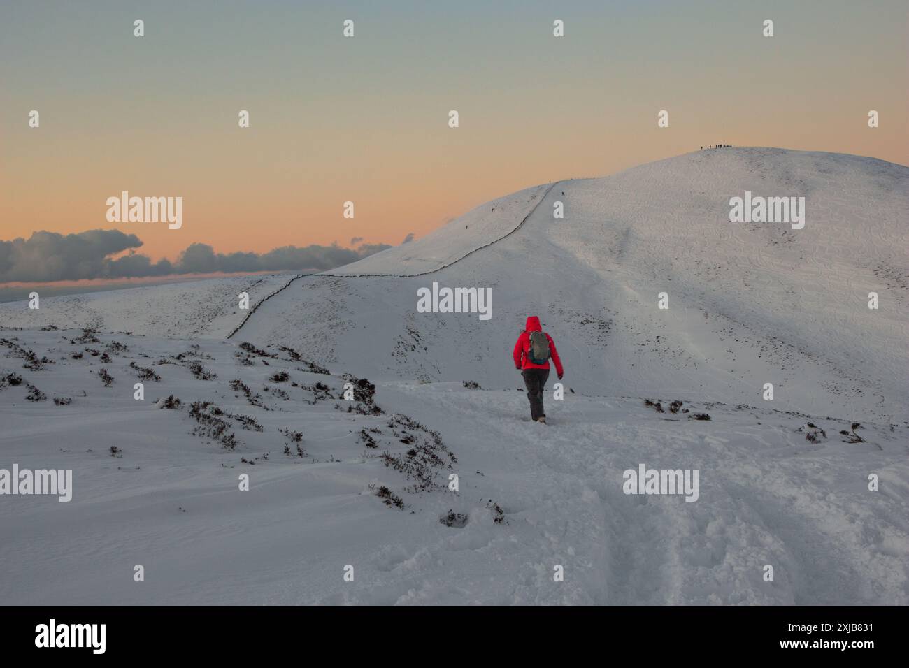 Persona che indossa una giacca rossa, uno zaino e abiti invernali, escursione fino alla vetta della montagna innevata sulle colline di Pentland, vicino a Edimburgo, Scotlan Foto Stock