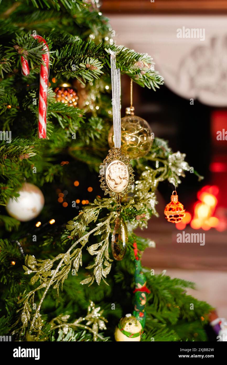 Primo piano di un ornamento natalizio d'epoca appeso a un albero decorato con un caminetto sullo sfondo Foto Stock