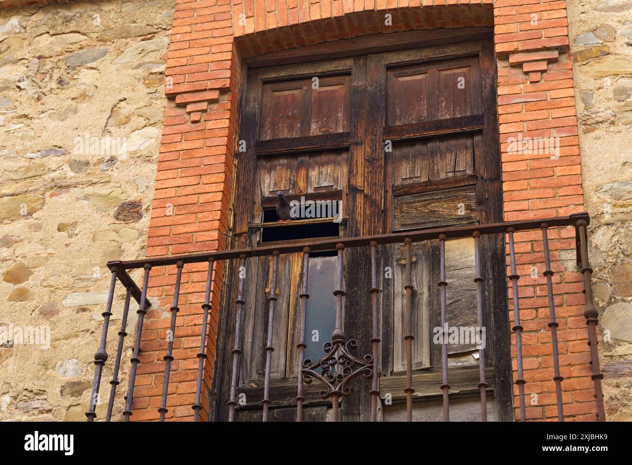 Un balcone in legno intempestivo con una ringhiera in ferro arrugginito e un piccione solitario arroccato sul bordo, affacciato sulle affascinanti strade di Astorga, Spagna. Foto Stock