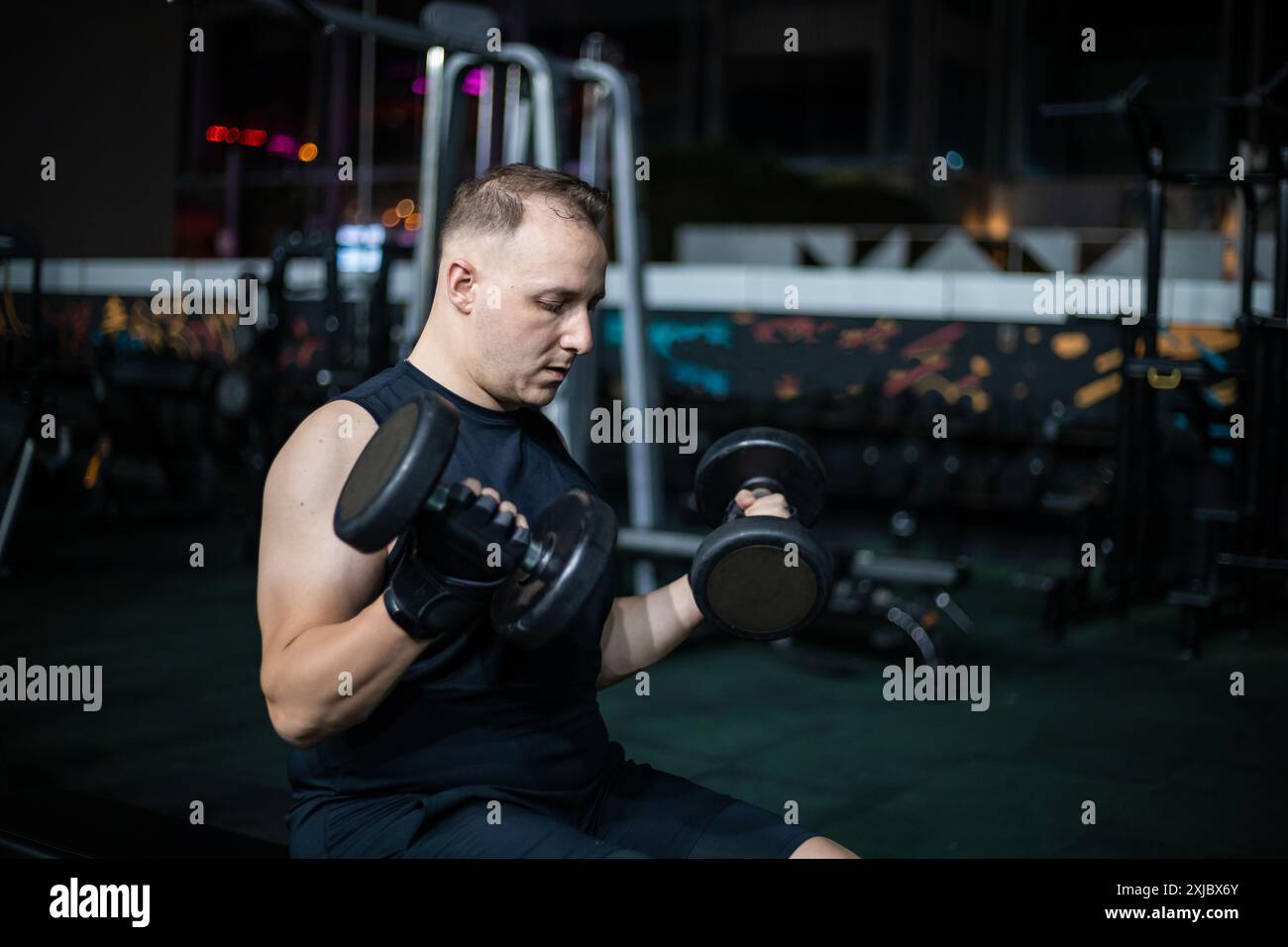 Un uomo con una canotta nera solleva i manubri mentre si allena in palestra. Foto Stock