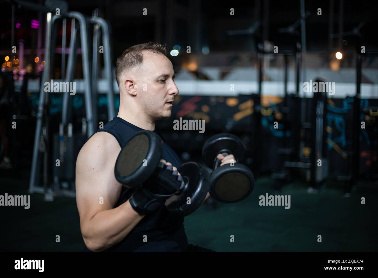 Un uomo solleva pesi mentre si allena in una palestra poco illuminata. Foto Stock