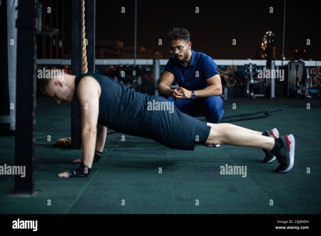 Un uomo esegue push-up mentre un allenatore osserva e osserva la sua forma. Foto Stock