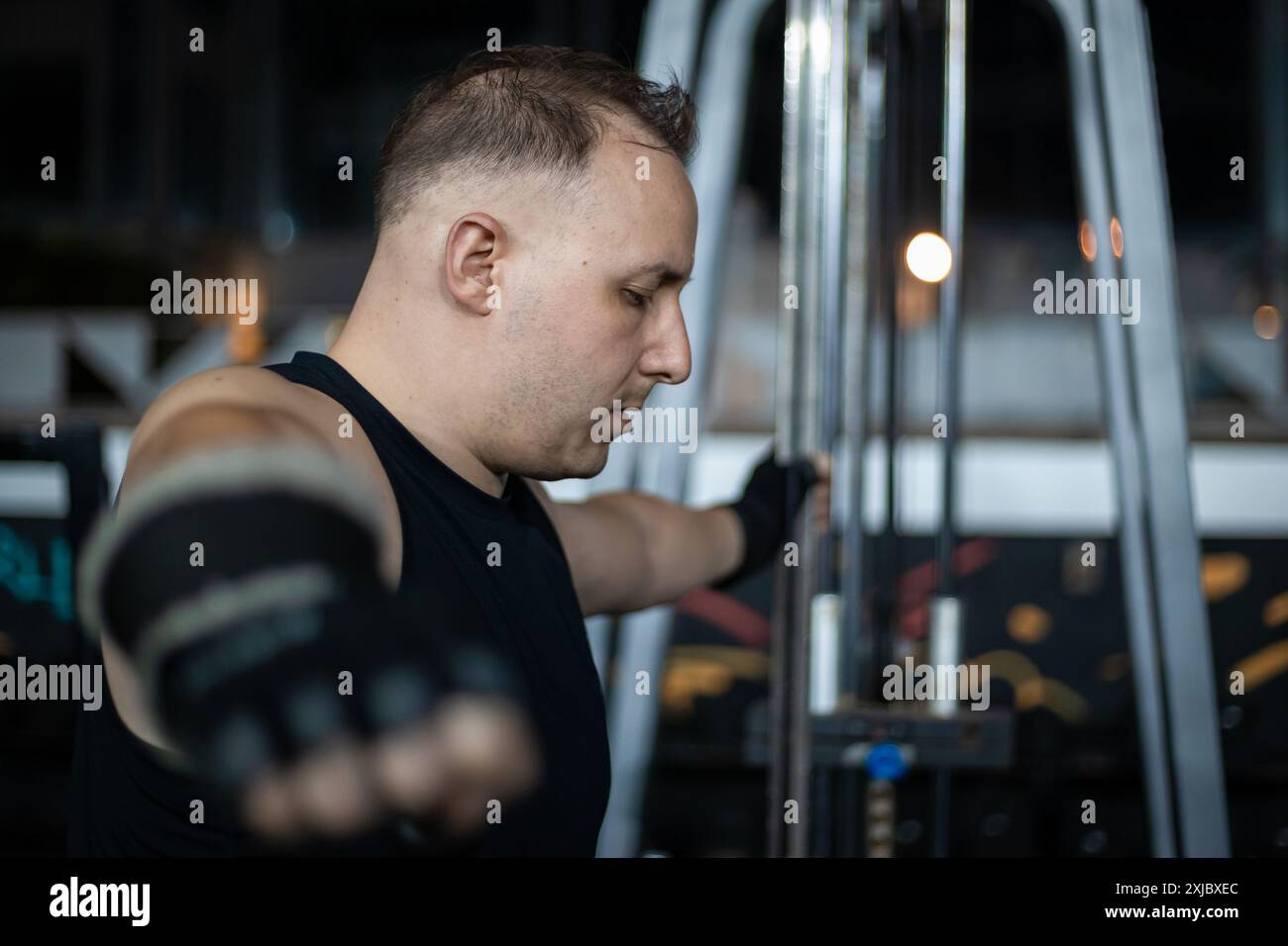 Un uomo che indossa una canotta nera e guanti neri si sta allenando su una cabinovia in palestra. Foto Stock Un uomo che indossa una canotta nera e guanti neri si sta allenando su una cabinovia in palestra. Foto Stock