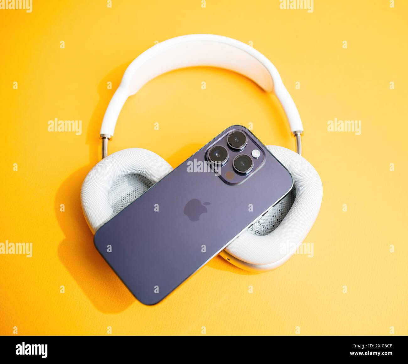 Parigi, Francia - 11 giugno 2023: Un iPhone Apple con tripla configurazione della fotocamera si appoggia su cuffie bianche su un vivace sfondo giallo, che presenta un design moderno e minimalista Foto Stock
