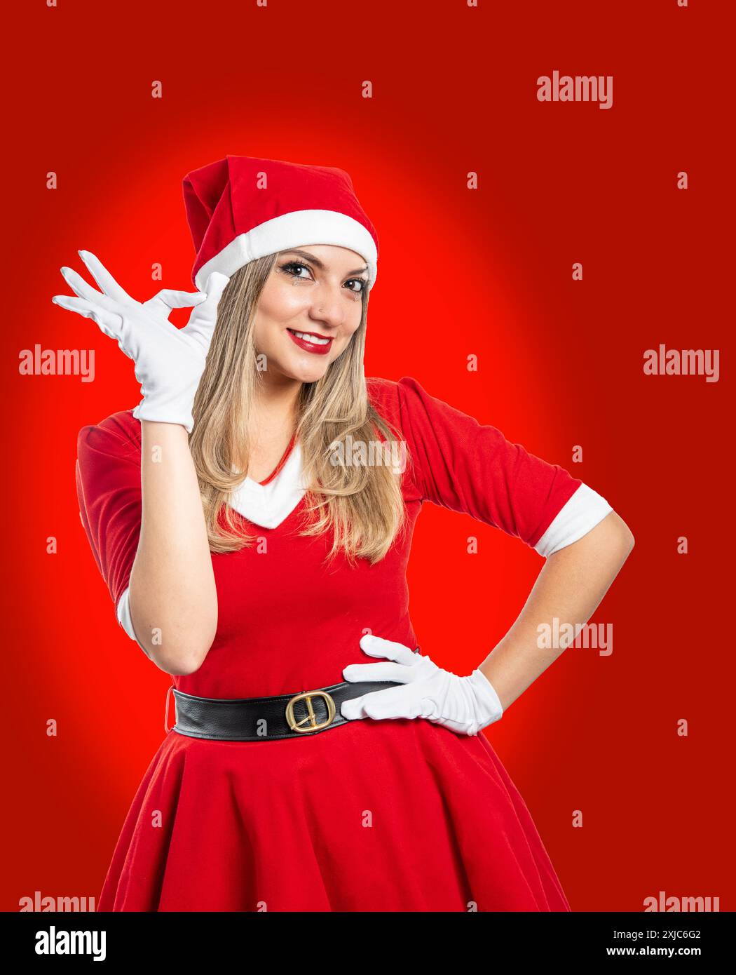 Il giovane babbo natale sorridente guarda la telecamera che fa un buon gesto di approvazione isolato su sfondo rosso Foto Stock