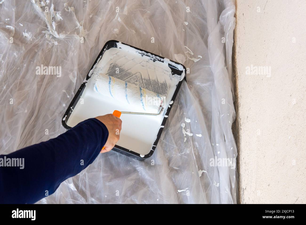 Primo piano delle mani utilizzando un rullo per pittura e della vernice bianca sul vassoio per vernice Concetto di miglioramento della casa e di verniciatura della casa. Foto Stock
