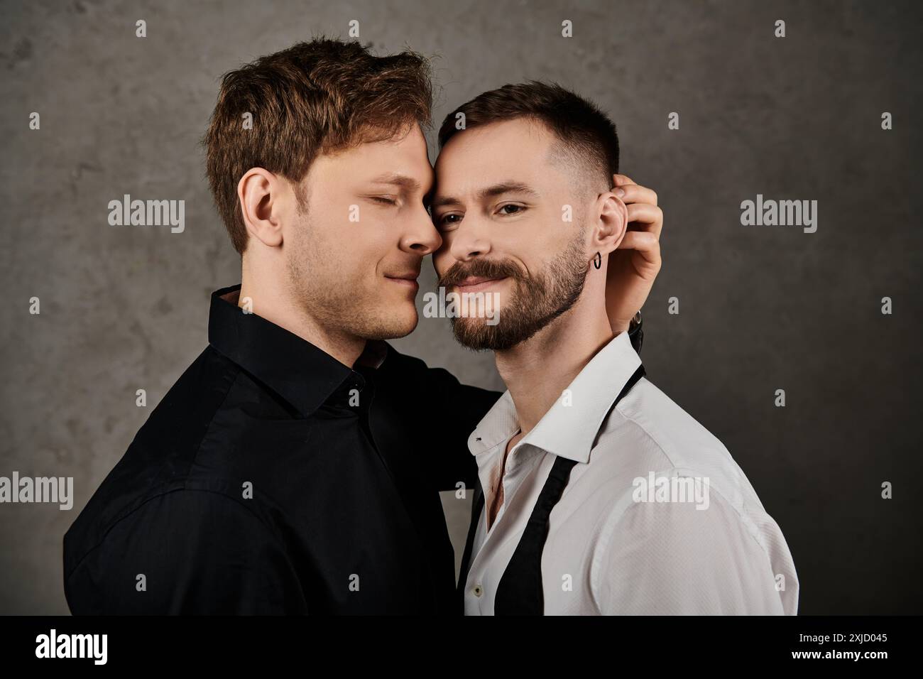 Una coppia gay in abiti eleganti, abbracciata in un ambiente da studio. Foto Stock