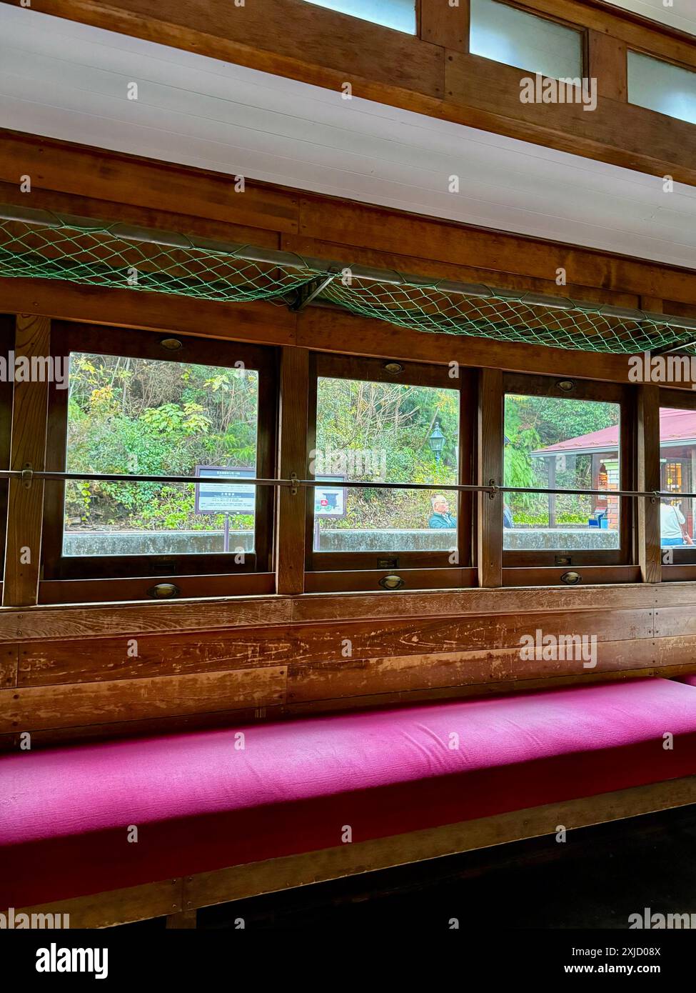 Vista interna di un treno d'epoca in legno con sedili e finestre imbottiti rossi che si affacciano su un lussureggiante paesaggio verde. Foto Stock