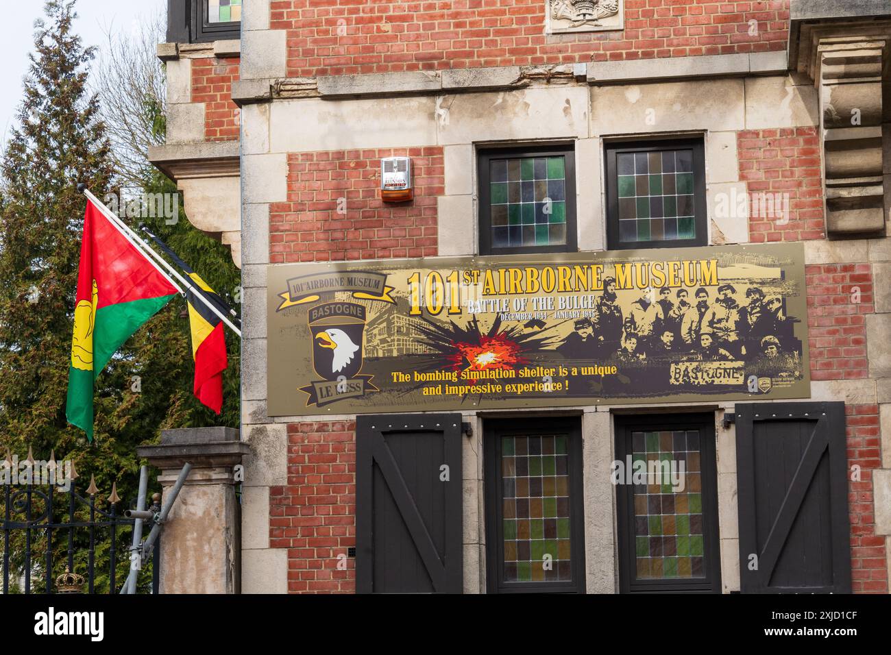 Insegna esterna per il Museo della 101ª Aviotrasportata a Bastogne, Belgio, con bandiere americane e belgiche che fiancheggiano l'ingresso. Foto Stock