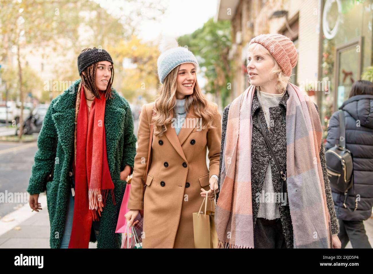 Gruppo di diverse donne che passeggiano per la città in autunno. Amici di diverse etnie che indossano abiti autunnali alla moda e portano borse per la spesa. Scena d Foto Stock