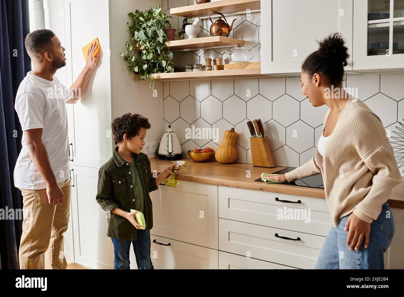 Un uomo e una donna afroamericani stanno pulendo energicamente la cucina insieme, mostrando amore e lavoro di squadra, con il figlio. Foto Stock