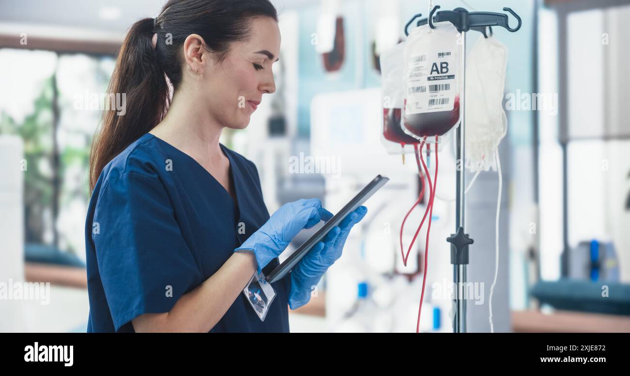 Infermiera donna che tiene il computer del tablet e controlla la sacca di sangue nel centro donazioni. Donna caucasica professionale che osserva il processo di donazione in Bright Hospital. Assistenza sanitaria e beneficenza. Foto Stock